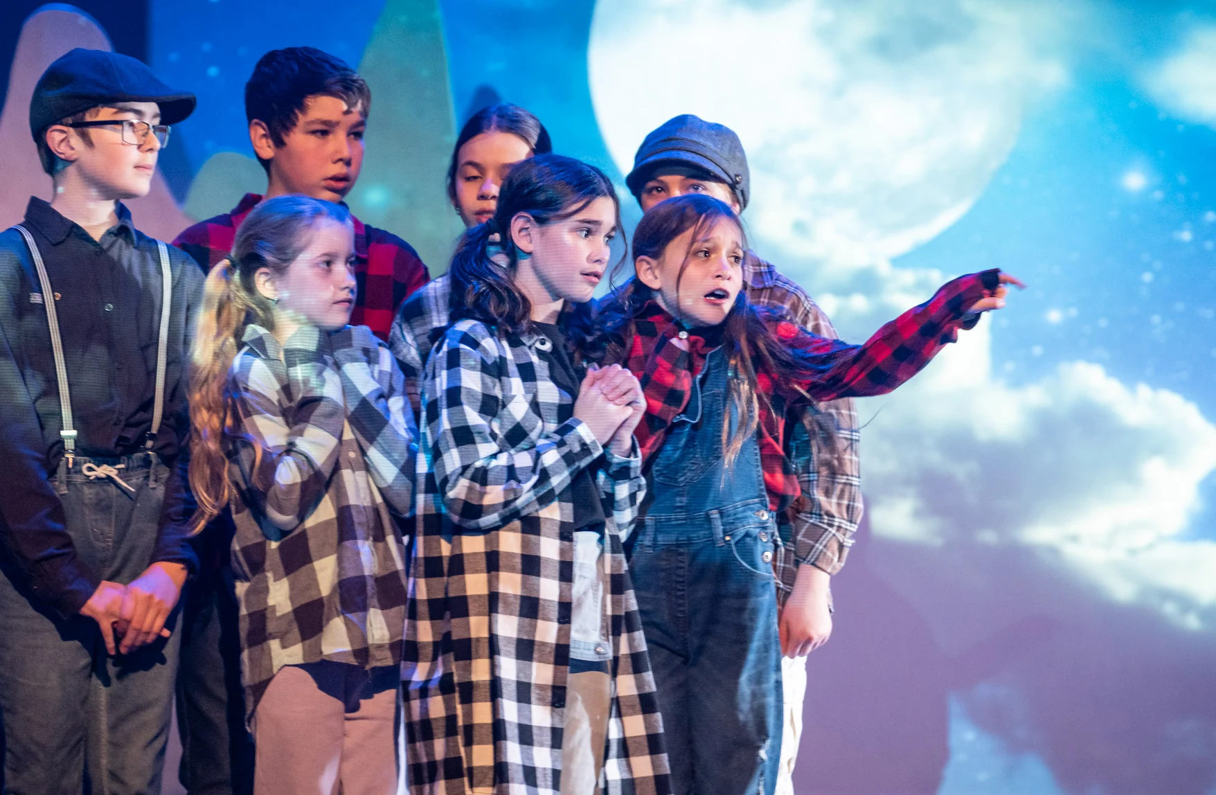 Troupe d'enfants sur une scène de théâtre avec un décor de lune